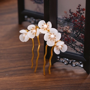 Detail of two gold U-shaped hairpins with white floral shell petals and small pearls