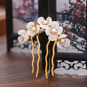 Detail of golden U-shaped hair fork with white flowers and pearls against a wooden screen