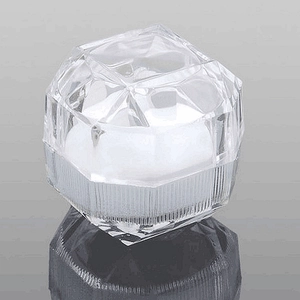 Transparente facettierte Ringbox aus Kunststoff mit weißem Kissen auf reflektierendem Boden