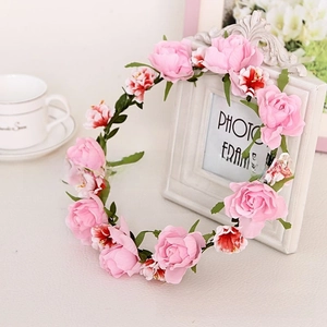 Detail of pink fabric roses and green leaves on a floral crown against a white frame