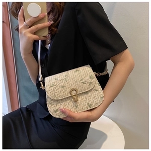 Detail of beige woven crossbody bag featuring green floral embroidery and gold buckle