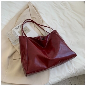 Close-up of wine red glossy wrinkled leather tote bag displayed on chic beige fabric
