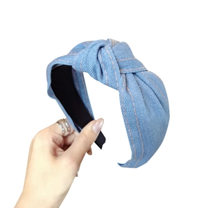 Denim knotted headband in light blue with orange stitching shown on a white background