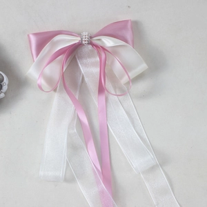 Close-up of pink and cream bow hair clip with pearls, rhinestones and long satin ribbons