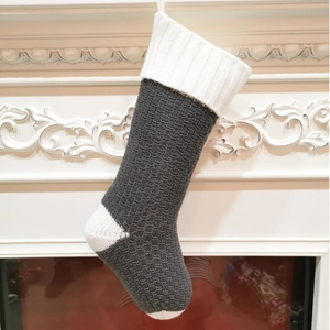 Close-up of grey knitted Christmas stocking with leaf cable pattern on a white fireplace