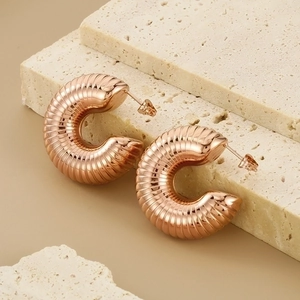 Detailed close-up of rose gold C-shape hoop earrings with textured ribbed design on stone