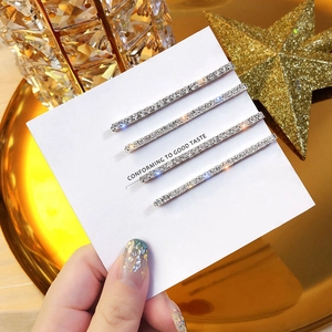 Close-up of four silver rhinestone bobby pins displayed on a white card against a gold tray