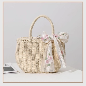 Detail of beige woven straw tote bag featuring a pink floral embroidered silk ribbon bow