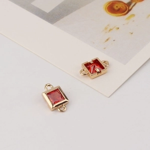 Close-up of golden geometric square connectors with faceted red zircon stones for jewelry