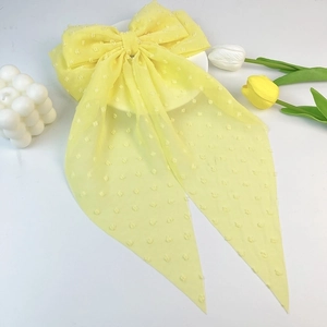 Detail of yellow chiffon bow hair clip with textured polka dots and long ribbons