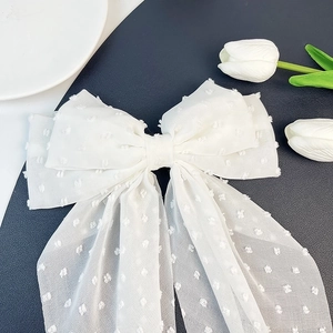 Detail of white chiffon oversized bow hair clip with textured polka dots and long ribbons