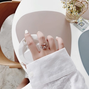 Close-up of a silver flower ring with blue crystals worn on hand in a cozy cafe setting