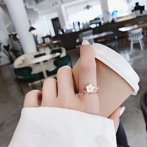 Rose gold adjustable ring featuring a crystal flower charm worn by a model holding a cup