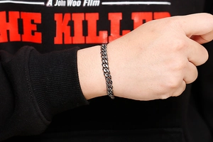Detail of a dark grey stainless steel cuban link bracelet worn on a male wrist