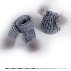 Close-up of grey knit baby hat and scarf set featuring dual faux fur pom-poms details