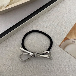 Close-up of a minimalist black elastic hair tie with a polished silver metal bow detail