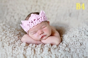 Close-up of a newborn wearing a pink knitted crown prop on soft textured beige fabric