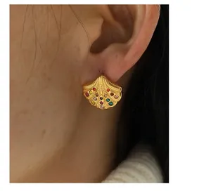 Detail of golden shell earrings with multi-colored gemstones on a female model