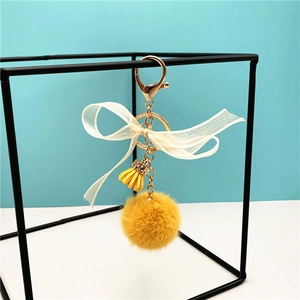 Close-up of yellow plush ball keychain with white ribbon bow and gold metal clasp detail