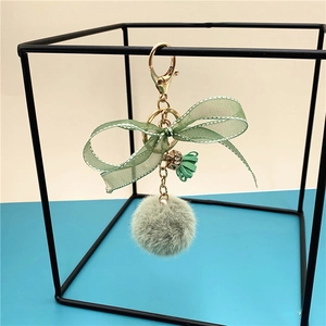 Close-up of green plush ball keychain with lace bow, golden clip and tassel detail