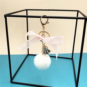 Detail of fluffy white pom-pom keychain with pink lace bow and grey tassel charm