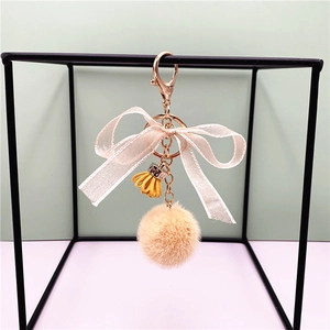 Detail of apricot faux fur pompom keychain with silk bow and gold metal clasp