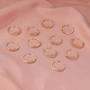 Detailed view of twelve gold adjustable zodiac letter rings on pink silk background