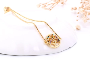 Detailopname van gouden levensboom armband met gekleurde stenen op wit keramiek bord