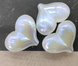 Macro detail of three pearlescent iridescent heart-shaped DIY resin craft beads