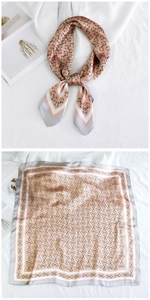 Detail view of a pink square silk scarf featuring golden horsebit and chain patterns