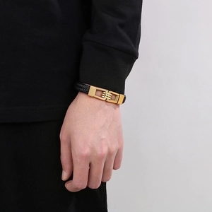 Detail of men's braided leather bracelet in black with golden metal clasp on wrist