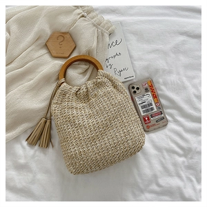 Detail of hand-woven beige straw bag with round wooden handle and stylish tassel charm