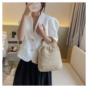 Detail of hand-woven straw bag featuring a wooden circular handle and stylish side tassel