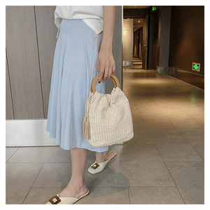 Detail of woven straw handbag featuring a round wooden handle and stylish side fringe