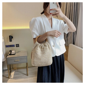 Detail of woven straw handbag featuring a round wooden handle in a lifestyle setting