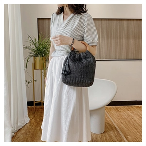 Detail of black woven straw bag featuring circular wooden handle and tassel decoration