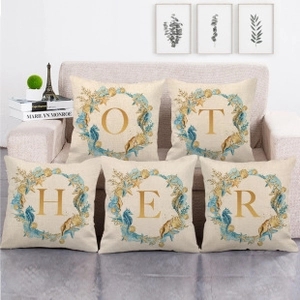 Detail of five beige linen pillow covers with gold alphabet letters O T H E R on a sofa