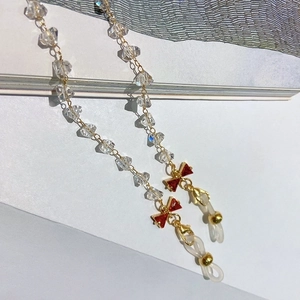 Detail of crystal eyewear chain featuring a red zircon bow and gold lobster clasp