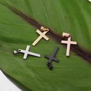 Polished stainless steel cross pendants in silver, gold, rose gold and black on a green leaf