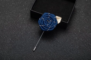 Close-up of a navy blue fabric rose lapel pin with gold trim in a black gift box