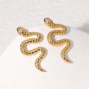 Macro shot of gold snake-shaped stud earrings with detailed scale texture on white stand