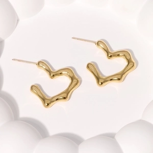 Detailed view of gold wave-patterned heart stud earrings on a white relief surface