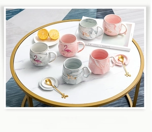 Flat lay of pink and grey marble ceramic mugs with gold spoons on marble table