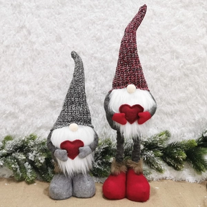 Close-up of knit gnomes with white beards holding red hearts on snowy pine decor
