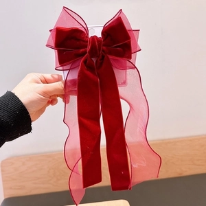 Close-up of a large burgundy velvet hair bow with elegant sheer ribbons held by hand