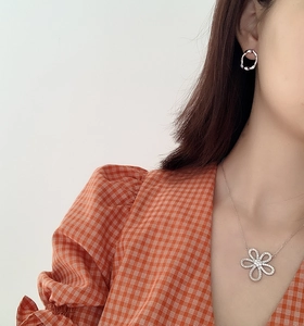 Close-up of irregular sterling silver earring and floral pendant necklace on a model
