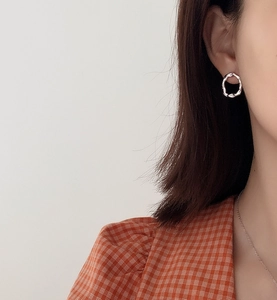 Close-up of irregular textured silver stud earring worn by model on plain background