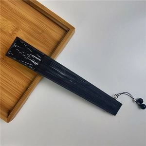 Close-up of a closed black bamboo folding fan with matching bead tassel on a wooden tray