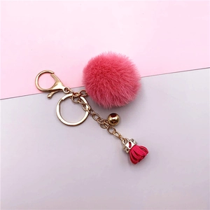 Detail of pink faux fur pompom keychain with golden bell and tassel pendant accessory