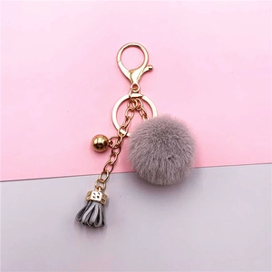 Cute gray faux fur pom pom keychain with gold chain tassel and bead on dual-tone background
